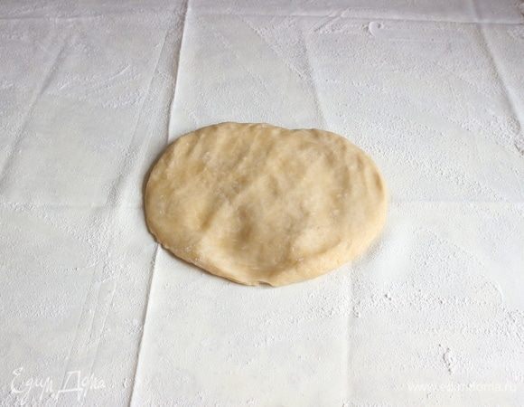 Положить лепешку из теста на скатерть, посыпанную мукой.
