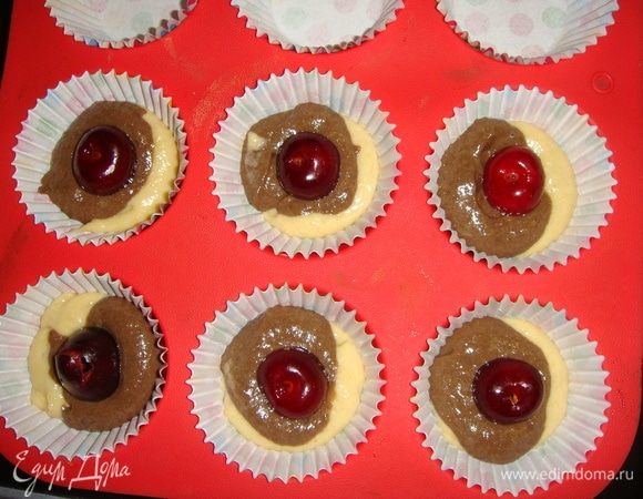 В формы для кексов вложить бумажные капсулы. Выкладываем тесто чайной ложкой, чередуя темное и светлое. В середину положить по одной черешне без косточки.