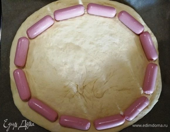 Подошедшее тесто руками растягиваем в круг (лучше сразу на противне). По краю выкладываем сосиски.