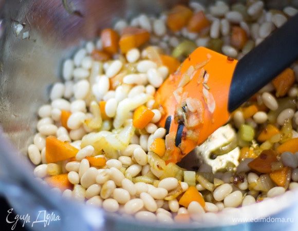 К овощам добавить фасоль, влить бульон и довести до кипения. Затем добавить мелконашинкованную капусту, довести до кипения, дать покипеть 2–3 минуты и отправить кастрюлю с супом в духовку (200°C) на 15 минут.