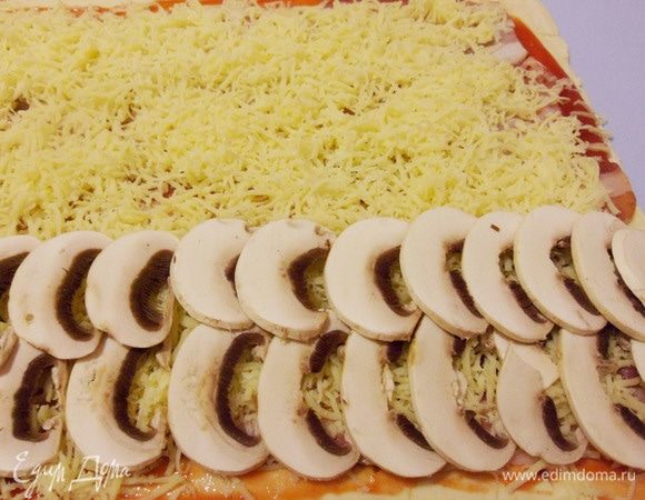 С большего края уложить тонкие ломтики шампиньонов.