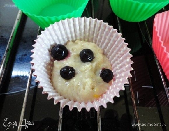 Добавить просеянную муку с разрыхлителем и замесить ложкой жидкое тесто. В формочки выложить небольшое количество теста, несколько ягод и сверху еще немного теста. Естественно, формочки заполняем на 1/3, оставляя место для подъема.