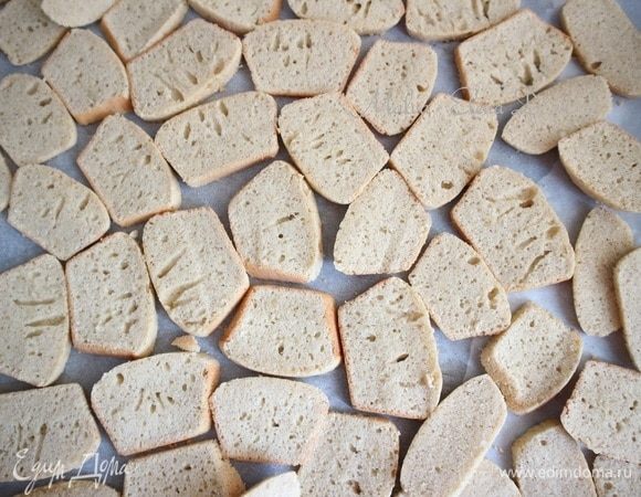 Дать остыть. Нарезать тонкими пластинами острым ножом. Противень застелить бумагой для выпечки. Положить на противень в один слой кусочки выпечки.