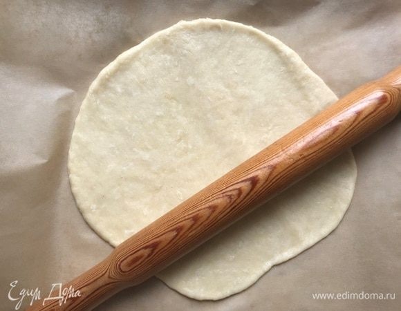 Приготовить тесто. Смешать муку, соль и соду. В мерный стакан налить кипяток и масло, добавить уксус, перемешать и влить в миску с сухими ингредиентами. Замесить мягкое тесто, затянуть в пленку и оставить на 30 минут. Раскатывать тесто удобно сразу на листе пекарской бумаги.
