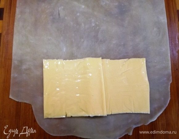 Возьмем одну заготовку и раскатаем ее очень тонко, чтобы просвечивалась рабочая поверхность. На край выкладываем пластинки сыра.