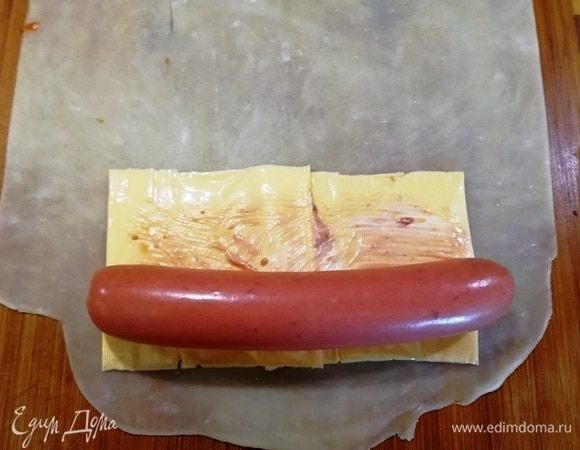 Смазываем сыр небольшим количеством майонеза и кетчупа. Сверху укладываем сосиску.