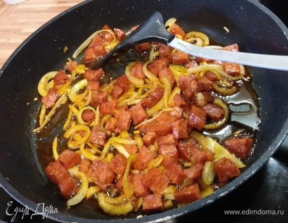Лук очистить и нарезать на стрелки, перцы очистить и нарезать произвольно, чоризо нарезать мелким кубиком. В сковороде разогреть небольшое количество растительного масла и пассеровать лук с чоризо. Параллельно поставить вариться макароны (у меня лингуини).