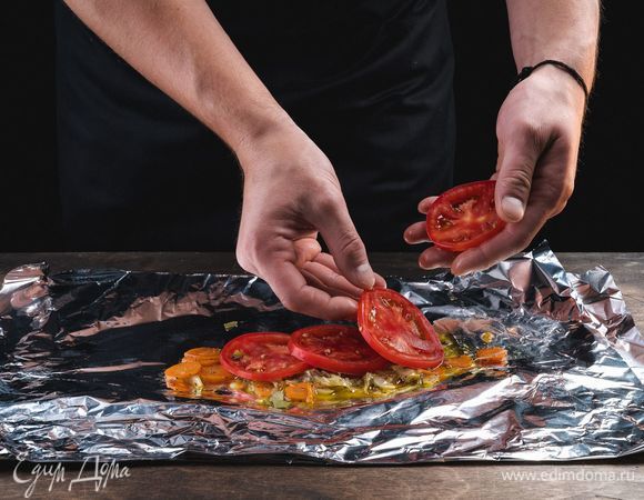 Выложите приготовленные овощи в конвертик из фольги, сверху положите часть нарезанного помидора.