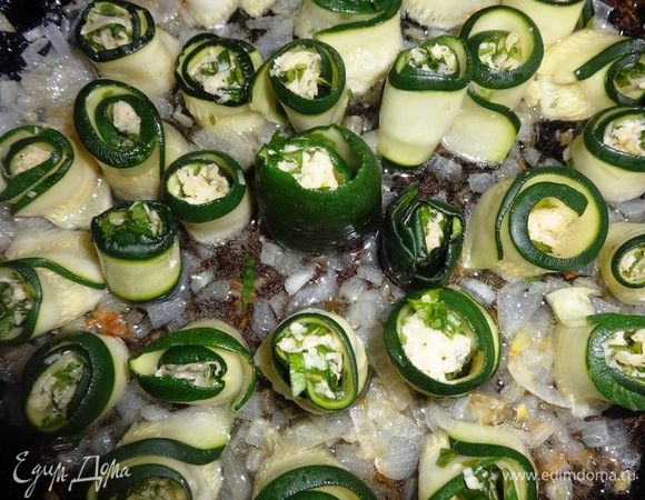 В сковороду к обжаренному луку выложить рулетики цукини зеленой каемочкой вверх.