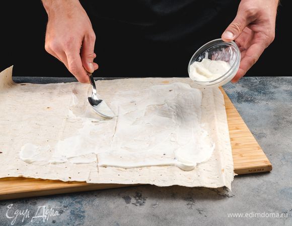 Разверните лаваш и смажьте греческим йогуртом. Края лаваша оставьте без йогурта, так будет легче сворачивать рулет.