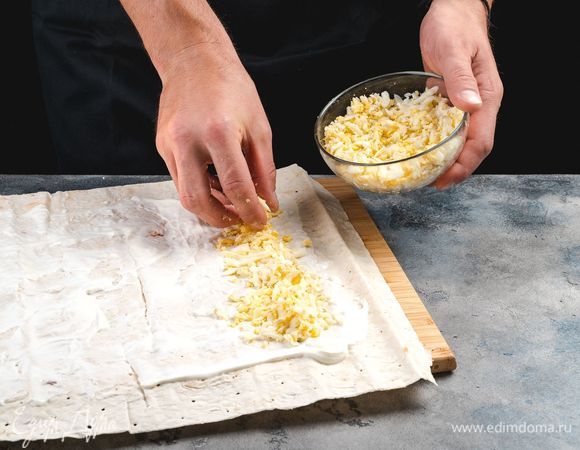 Отварите куриные яйца, очистите и натрите на крупной терке. Сформируйте из них плотную вертикальную полоску на лаваше.