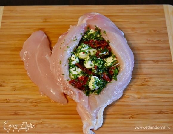 Куриное филе выложить на доску, отогнуть малое филе, по центру разрезать грудку вдоль не до конца. Справа и слева от разреза ножом сделать разрезы вглубь, формируя «кармашки». Старайтесь не разрезать филе насквозь. Начинку разделить на две части. Нафаршировать филе.