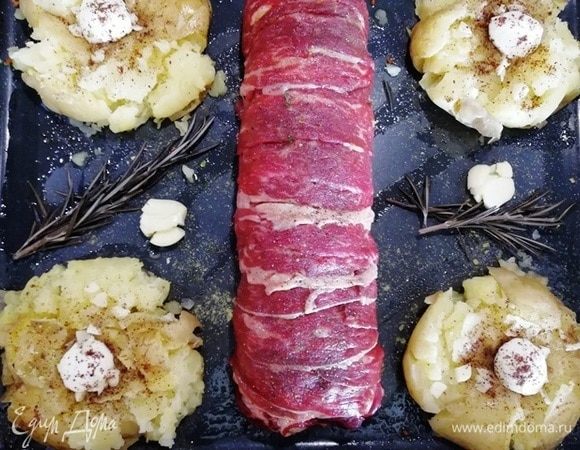 Придавливаем картофель толкушкой или плоской стороной широкого ножа. В центр картофелины кладем шарик моцареллы, чеснок, солим, перчим и сбрызгиваем маслом. В центр противня укладываем вырезку в беконе. Отправляем в духовку на 12–15 минут, температура — 190°C.