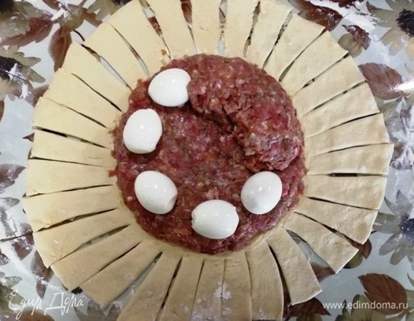 На фарш выкладываем яйца и облепляем их фаршем, чтобы яйца были полностью закрыты. Свободные края теста надрезаем по кругу.
