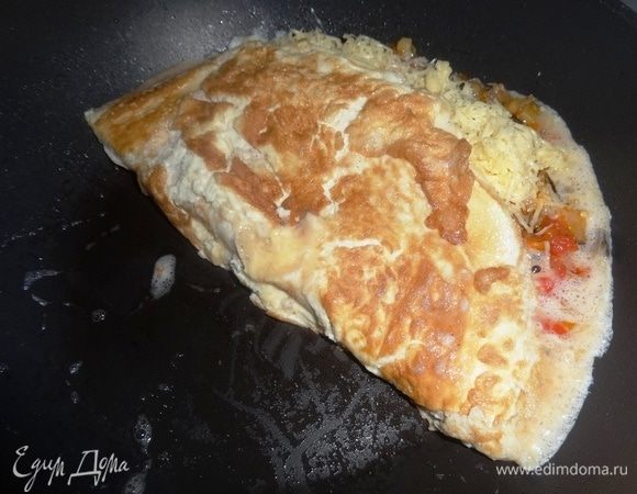 Аккуратно, с помощью двух лопаток, завернуть свободный от начинки край омлета на половину с начинкой. Накрыть сковороду крышкой и жарить на небольшом огне еще пару минут.