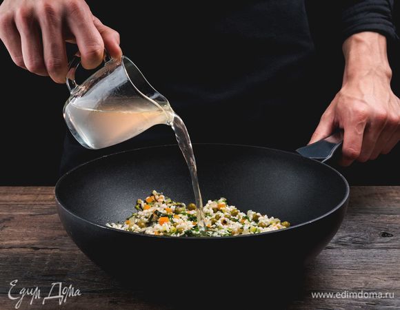 Начинайте вводить теплый овощной бульон. Вливайте в сковороду по одному половнику и ждите, пока он полностью впитается. На это уйдет примерно 20–30 минут. Рис должен дойти до состояния аль-денте.<br />
 