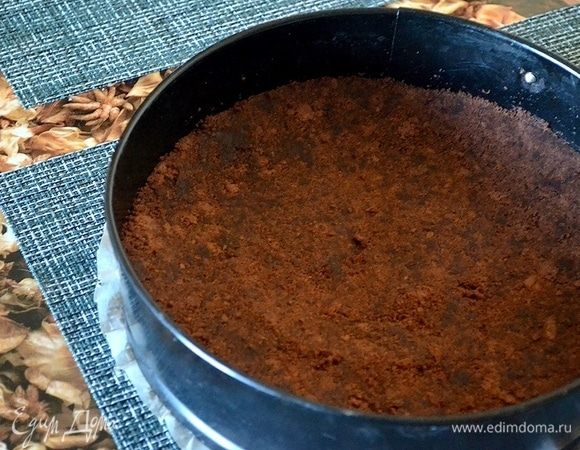 Готовим основу из шоколадного печенья и сливочного масла. Измельчаем печенье, смешиваем с маслом. На дно разъемной формы кладем лист пергамента. Выкладываем основу для чизкейка и утрамбовываем дно и стенки. Форму ставим в холодильник на час.