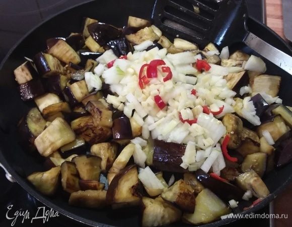 Разогреть масло в большой сковороде и обжарить баклажаны до золотистого цвета. Чаще мешайте, чтобы не подгорели. Добавить мелконарезанный лук, чеснок и перец чили, обжарить вместе еще минуту.