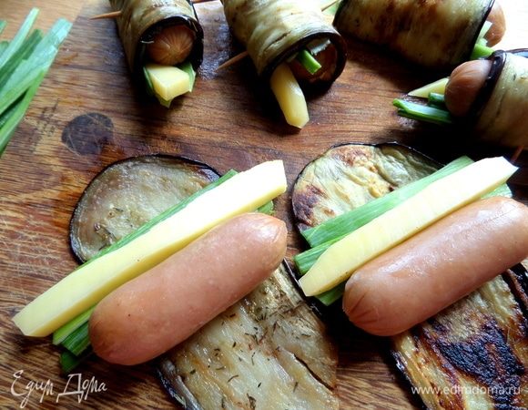 На пластинку баклажана положить брусочек сыра, 3 перышка лука и сосиску. У меня — местные детские известной фирмы. И вообще, считаю, если уж покупать сосиски, то только детские, к ним наиболее повышенные требования при проверке.