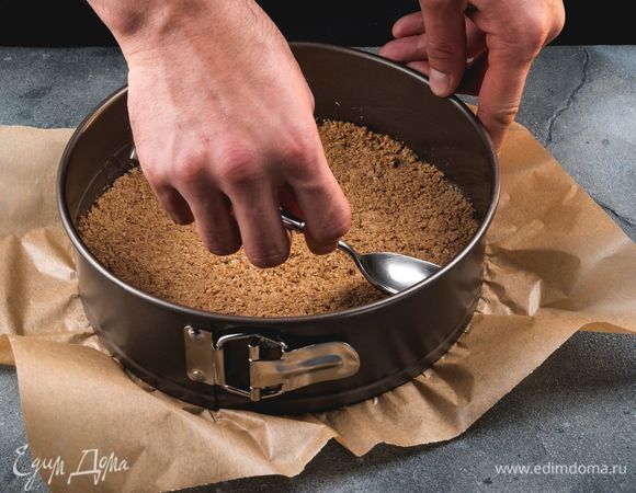 Подготовьте форму для выпекания: застелите ее пергаментом. Выложите в форму массу и хорошо равномерно утрамбуйте. Поставьте в холодильник на 15 минут.<br />
 