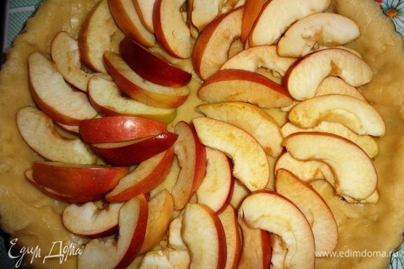 С помощью скалки перенести тесто в форму, аккуратно уложить по бортикам, излишки обрезать. На дно теста выложить дольки яблок, оставив небольшую часть долек.