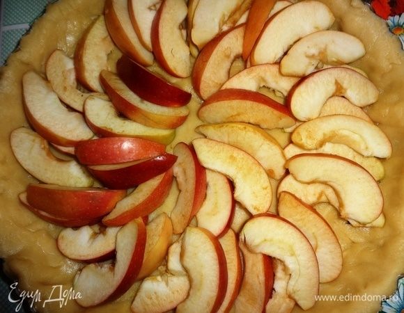 С помощью скалки перенести тесто в форму, аккуратно уложить по бортикам, излишки обрезать. На дно теста выложить дольки яблок, оставив небольшую часть долек.