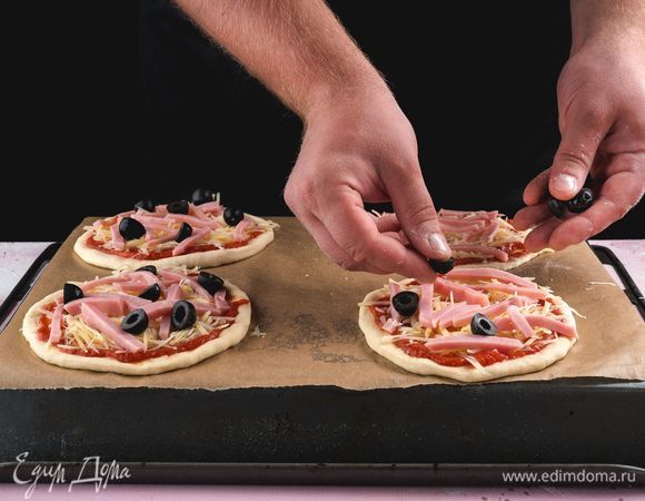 Противень застелите пергаментом, выложите заготовки. Каждый кружок теста смажьте соусом, посыпьте сыром, положите немного ветчины, маслины. Оставьте заготовки на 30 минут.<br />