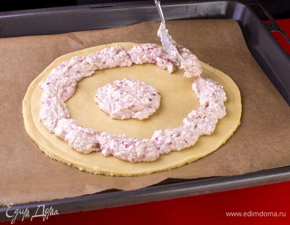 На листе пергамента раскатайте одну часть теста в круг. В центр выложите несколько ложек начинки. Остальную начинку выложите по краям в виде круга.<br />
 