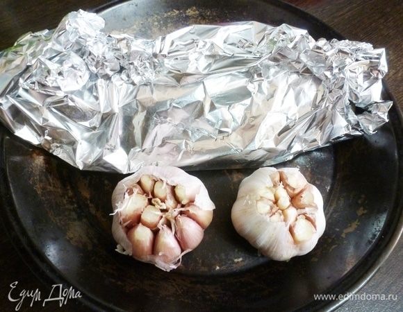 Затем завернуть рыбу в фольгу. Головки чеснока помыть, чтобы не было песка или земли, снять верхнюю шелуху. Срезать верхушку так, чтобы верх зубчиков открылся, полить оливковым маслом в разрезы. Отправить запекаться на 30–35 минут в духовку разогретую до 190°C.