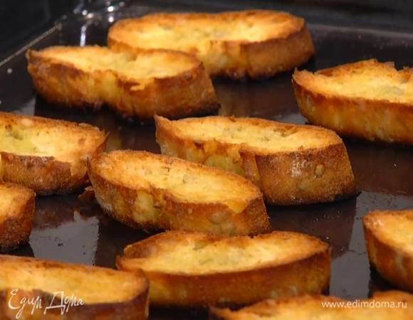 Багет нарезать тонкими ломтиками, выложить на противень, сбрызнуть оставшимся оливковым маслом и подсушивать в разогретой духовке 2–3 минуты.