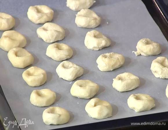 Сформировать из теста небольшие шарики, слегка расплющить их, сделав в центре небольшие углубления, и выложить на противень.