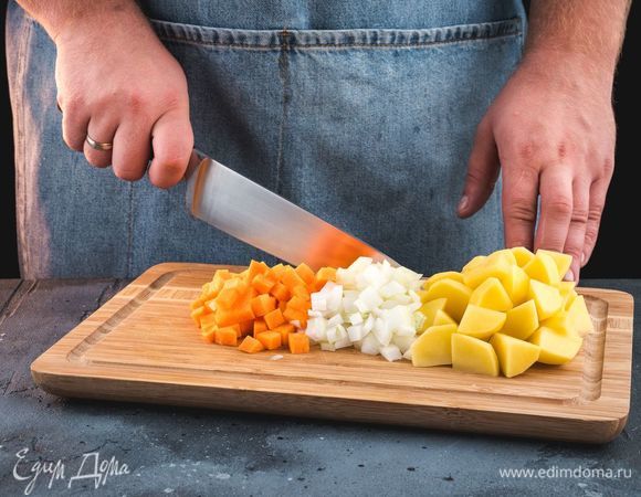 Куриный бульон поставьте на огонь и доведите до кипения. Очистите и нарежьте овощи: репчатый лук и морковь нарежьте мелкими кубиками, картофель — крупными.
