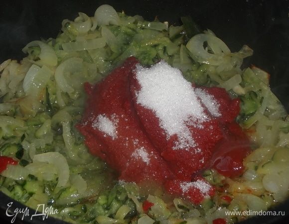 Томатную пасту добавить к луку с огурцами. Посыпать сахаром. Перемешать.