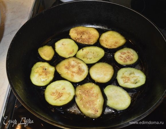 Включить плиту на средний огонь. Добавить растительное масло, разогреть и с двух сторон обжарить баклажаны, не закрывая крышку, до состояния мягкости.