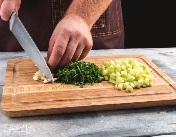 Огурцы очистите от кожицы и семян, мелко нарежьте мякоть кубиками. Нарежьте зелень, измельчите чеснок.