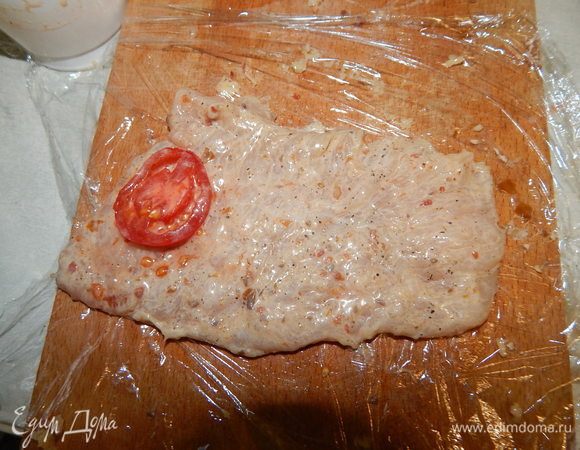 На пищевую пленку выложить филе, на него — кружочки помидоров.