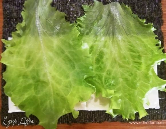 Лист нори выкладываем гладкой стороной вниз. На шероховатую сторону укладываем 2 пластинки плавленого сыра. На сыр выкладываем промытые и обсушенные листья салата.