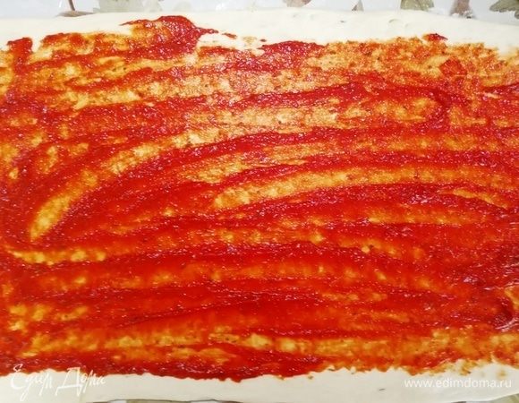 Затем раскатываем тесто в тонкий прямоугольник, наносим на него томатный соус.