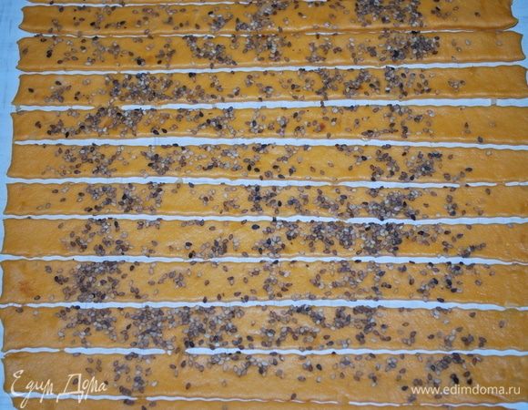 Раскатываем тесто, посыпаем его кунжутом, скалкой кунжут прижимаем к тесту. Разрезаем тесто на полоски шириной примерно 2 см.