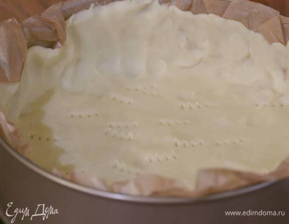 Охлажденное тесто поместить между двумя слоями бумаги для выпечки и раскатать в тонкий корж, затем вместе с нижним слоем бумаги уложить разъемную форму так, чтобы получились бортики, и часто наколоть вилкой.