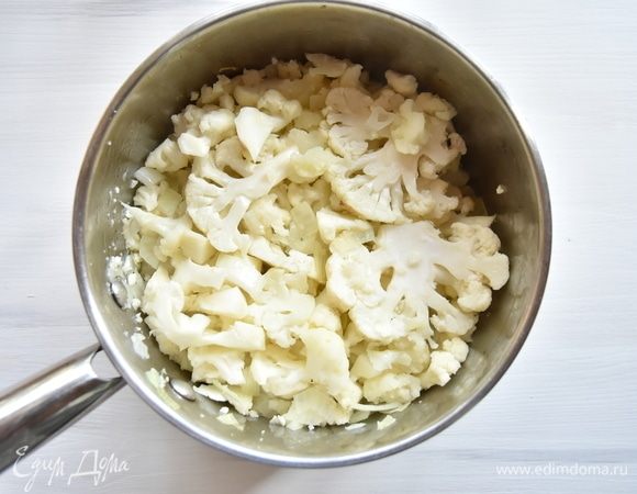 В сотейнике разогреть оливковое масло. Цветную капусту разобрать на соцветия и произвольно нарезать вместе с луком. Овощи выложить в сотейник, добавить немного бульона и потомить минут 5.