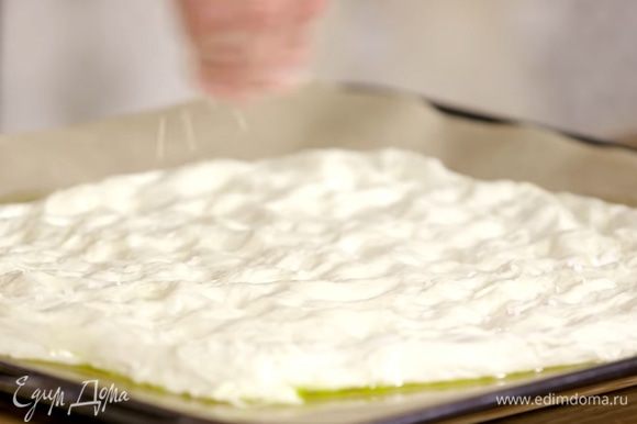Выстелить противень бумагой для выпечки, смазать ее оливковым маслом и равномерно выложить тесто, посыпать крупной солью и листьями розмарина.