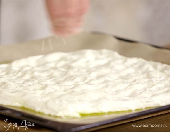 Выстелить противень бумагой для выпечки, смазать ее оливковым маслом и равномерно выложить тесто, посыпать крупной солью и листьями розмарина.