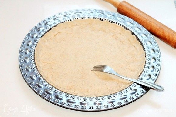 Обмять и тонко раскатать тесто на припыленной мукой столешнице в круг диаметром 26 см, и при помощи скалки перенести в смазанную маслом формочку (диаметр = 26 см). Проткнуть тесто вилкой в нескольких местах.