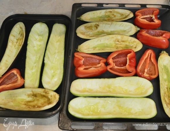 Включить духовку на 180°C. Баклажаны, кабачки и болгарский перец промыть, нарезать вдоль пополам, чтоб получились лодочки. У перца необходимо удалить сердцевину, вытряхнуть семена. У кабачков и баклажанов вырезать сердцевину и отложить (они нам пригодятся для начинки). На баклажанах и кабачках аккуратно сделать ножом порезы. Все овощи посолить, смазать маслом и отправить на 20 минут в духовку.