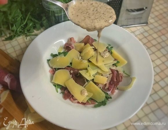 Салат раскладываем сразу порционно в тарелки. Сначала руколу, затем раскидываем прошутто, далее сыр и заправляем ореховым соусом — 2 ст. л. на одну порцию.