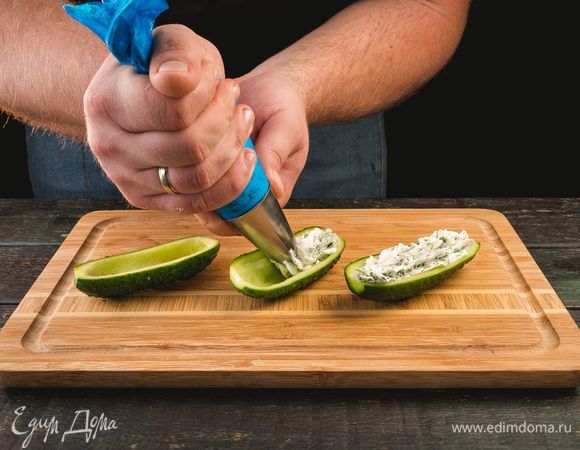 Огурец разрежьте пополам и сделайте лодочки, удалив сердцевины. В середину огуречной лодочки выложите начинку из сыра с зеленью.