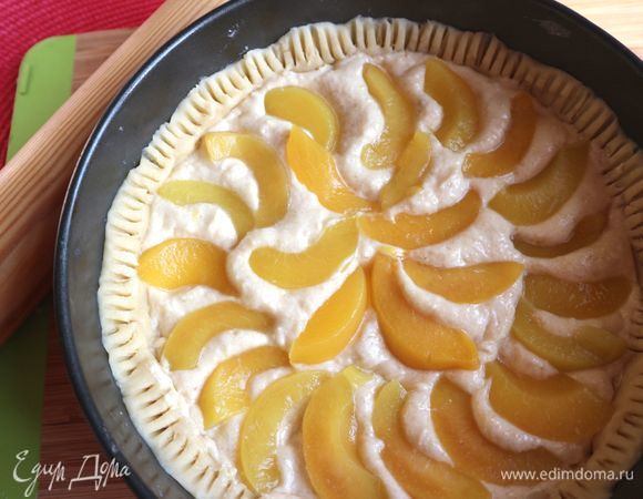 На основу из теста поместить равномерно крем, распределить по кругу дольки персиков, немного вдавливая их в крем. Зубцами вилки пройтись по края теста. Поставить в разогретую духовку на 40 минут. Температуру при этом надо убавить до 180°C.