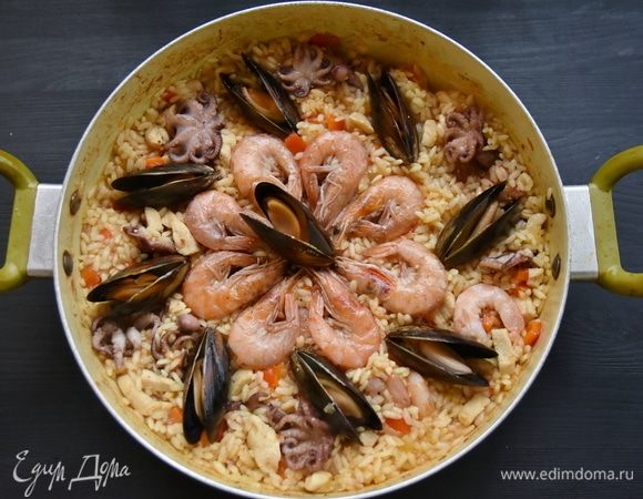 На максимальном огне, не накрывая сковороду крышкой, доведите блюдо до кипения и испарения влаги до уровня риса. На этом этапе выложите обжаренные морепродукты и зеленый горошек. Накройте сковороду крышкой, огонь уменьшите до минимального и 20 минут потомите блюдо до готовности риса.