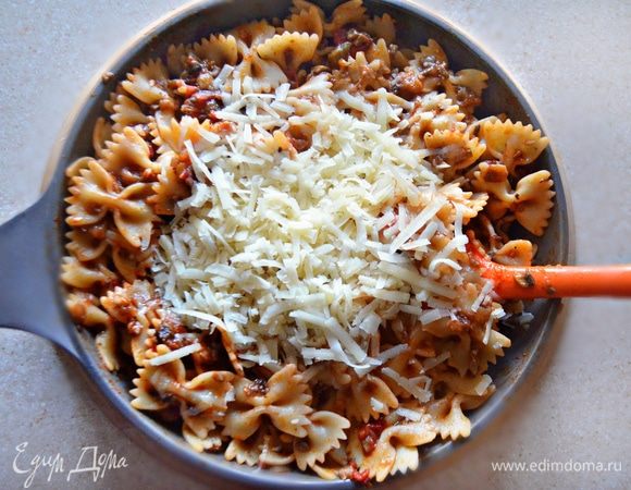 В сковороду с фаршем из баклажанов и грибов добавьте томатный соус, натертый сыр и пасту фарфалле, предварительно отваренную до состояния аль денте. Аккуратно перемешайте и прогрейте в течение 2–3 минут.